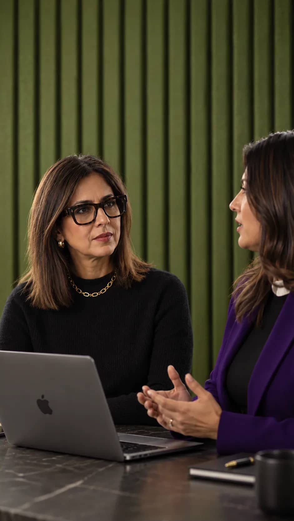 Two lawyers in discussion at a table with a laptop, in front of a green panelled wall
